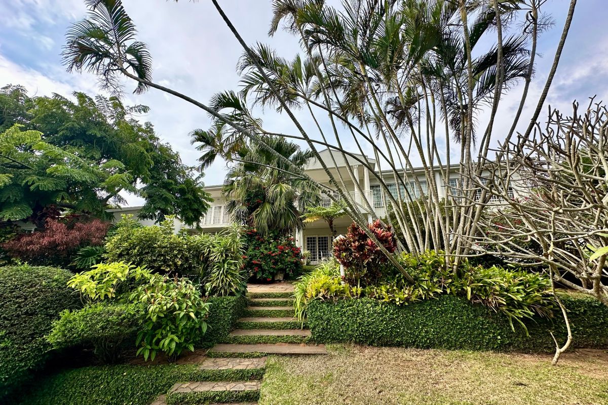 A lush, landscaped rear garden featuring stone steps leading up to a two-story residence with a balcony and french doors.