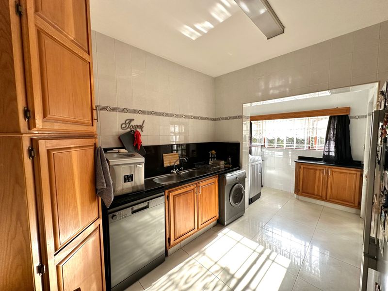 Functional scullery featuring timber cabinetry, granite countertops, double bowl sink, and tiled splashback, with integrated dishwasher and laundry appliance connections.