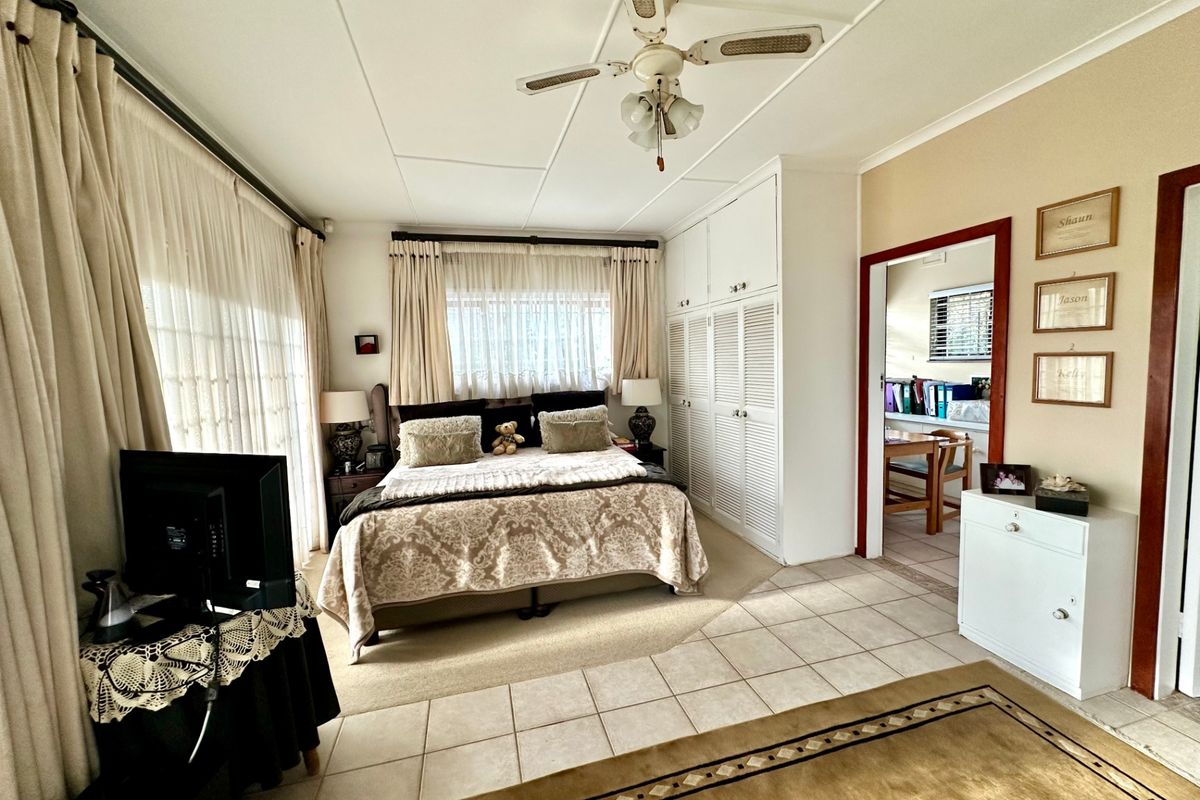 Spacious bedroom featuring tiled flooring, built-in cupboards, and a ceiling fan, with direct access to an adjoining room.