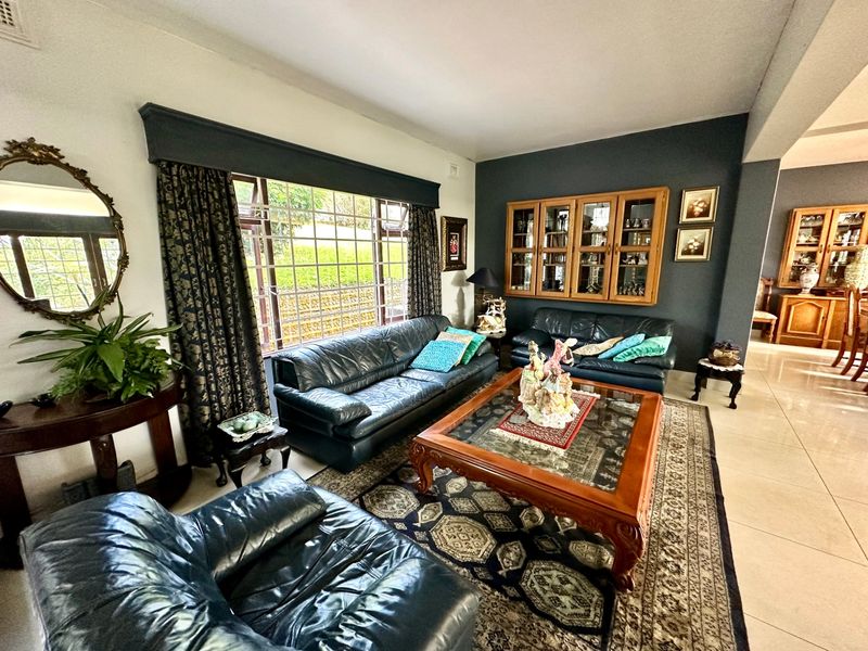 A spacious living room featuring tiled flooring, a large window with a pelmet, and built-in wooden display cabinetry against a dark accent wall.