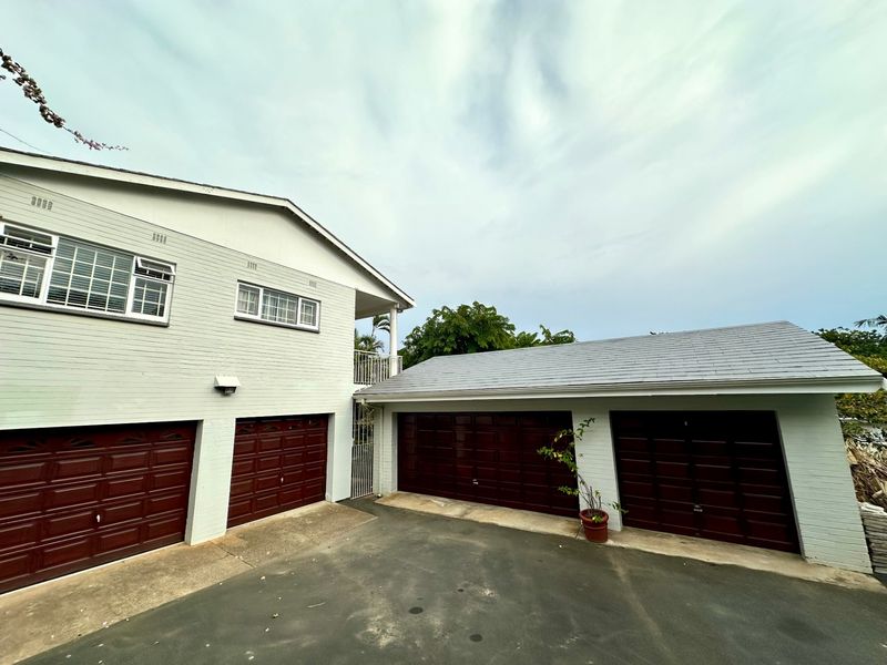 Exterior view of the property featuring a spacious four-car garage setup with a paved driveway and well-maintained painted brick facade.