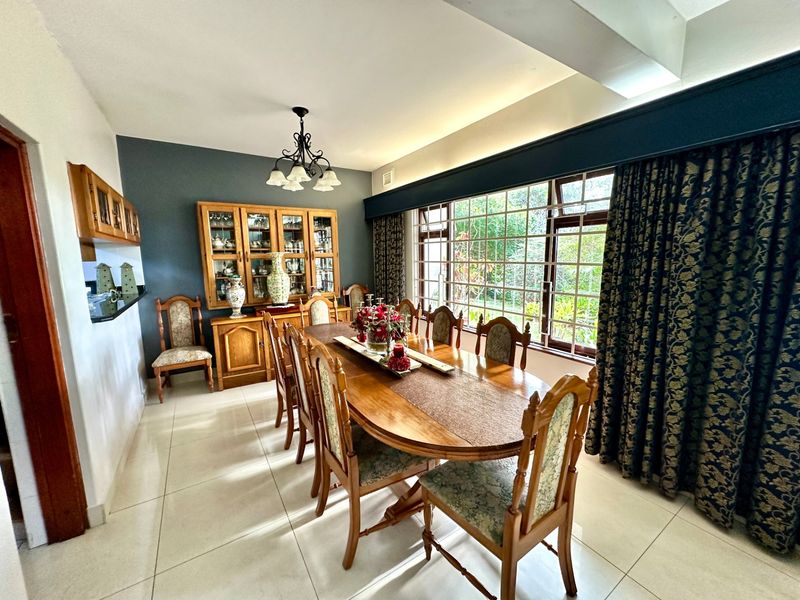 A spacious dining room featuring large grid-pattern windows, tiled flooring, and a built-in display cabinet, offering a bright and functional space for family meals.