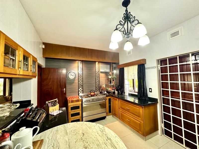 A functional kitchen featuring wooden cabinetry, granite countertops, a gas stove, and a decorative chandelier, offering a classic aesthetic with practical storage and workspace.