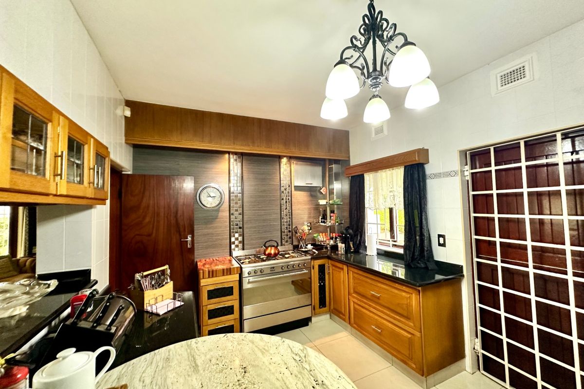 A functional kitchen featuring wooden cabinetry, granite countertops, a gas stove, and a decorative chandelier, offering a classic aesthetic with practical storage and workspace.