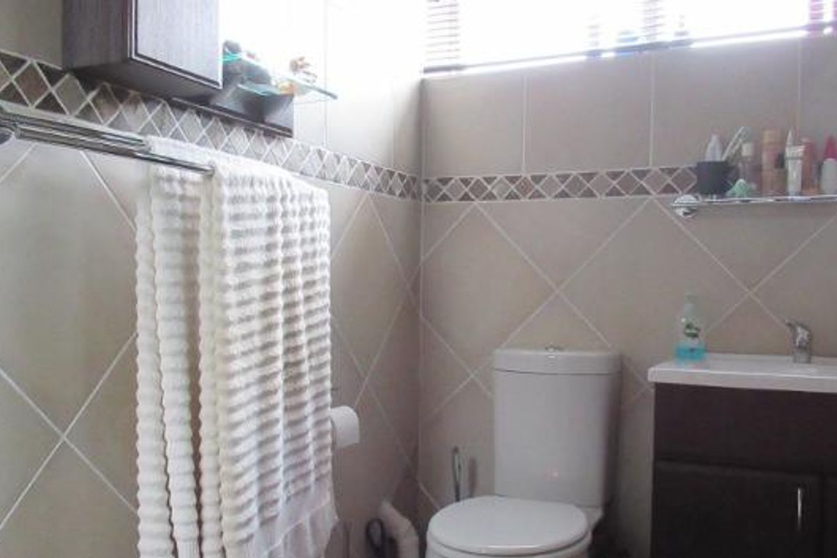 A compact bathroom featuring tiled walls, a vanity cabinet with a basin, a toilet, and a wall-mounted towel rail.