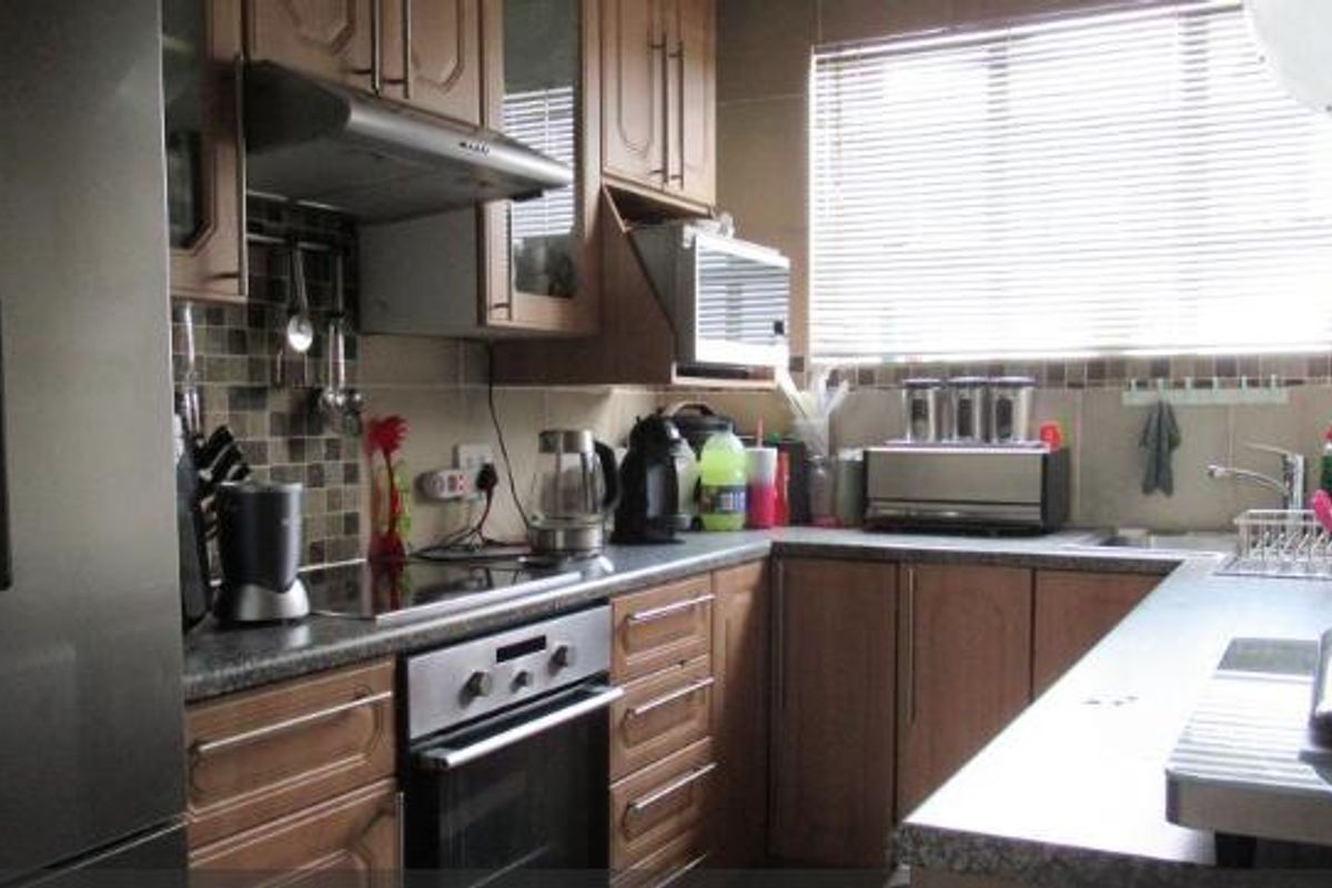 A functional kitchen featuring wood-toned cabinetry, a tiled backsplash, built-in oven, extractor fan, and stainless steel sink with ample counter space.