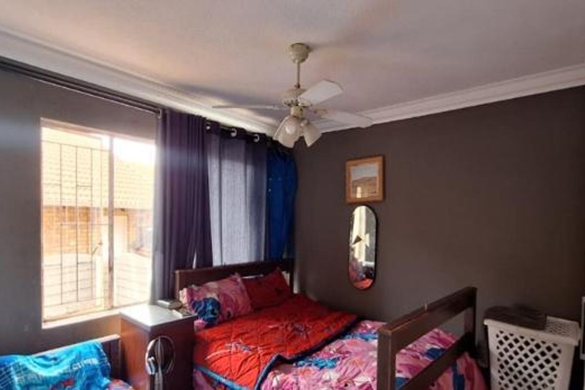 A standard bedroom featuring a ceiling fan, security bars on the window, and built-in storage cabinetry.
