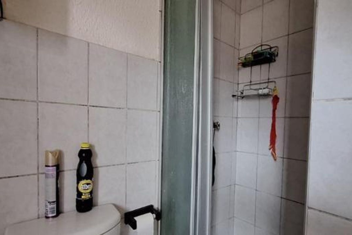 A functional bathroom featuring a shower enclosure and tiled wall finishes, showing signs of wear and dated fixtures.