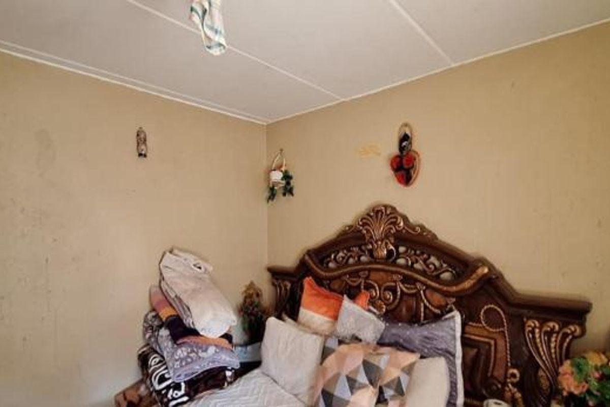 A bedroom featuring a large ornate headboard against walls that require repainting and surface repair.