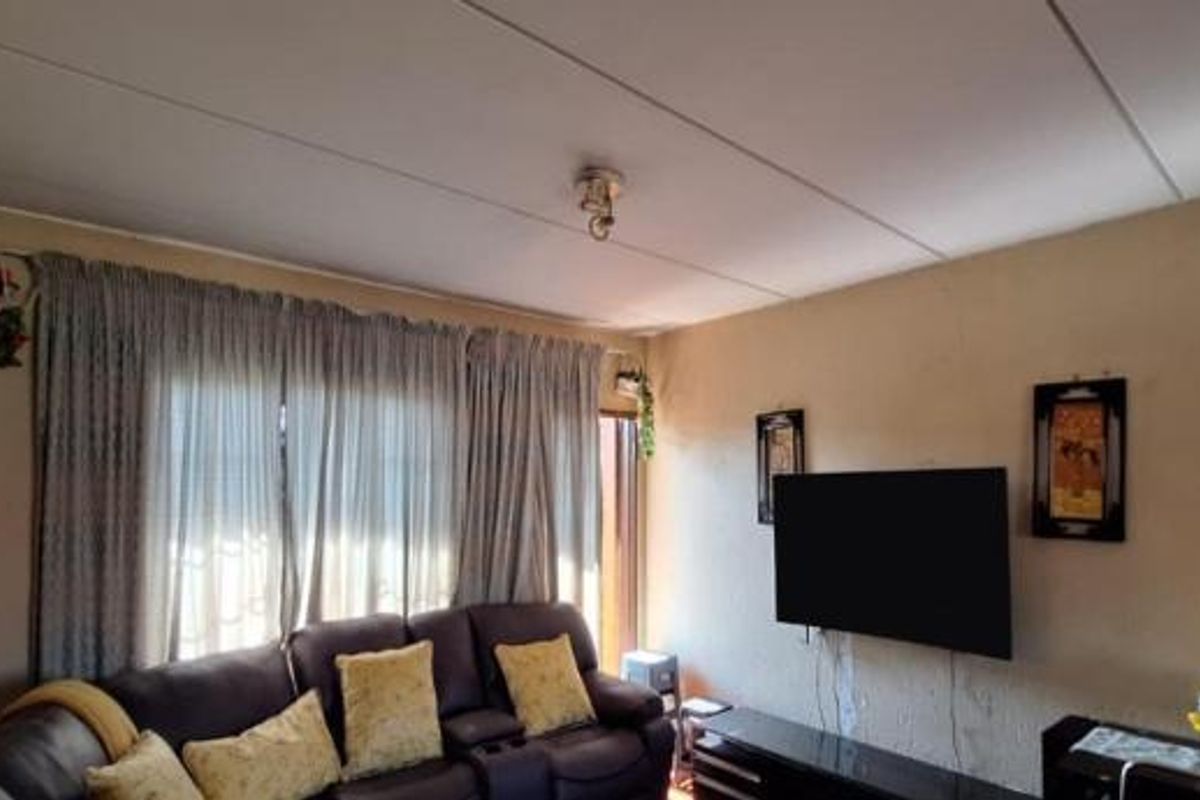 A living room featuring a drop ceiling and wall-mounted television, showing signs of wear on the wall surfaces.