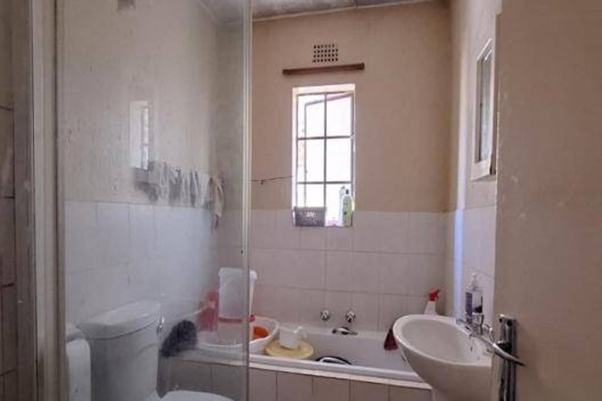 A dated bathroom featuring a shower enclosure, bathtub, pedestal basin, and toilet, with tiled walls and a small window for natural light.