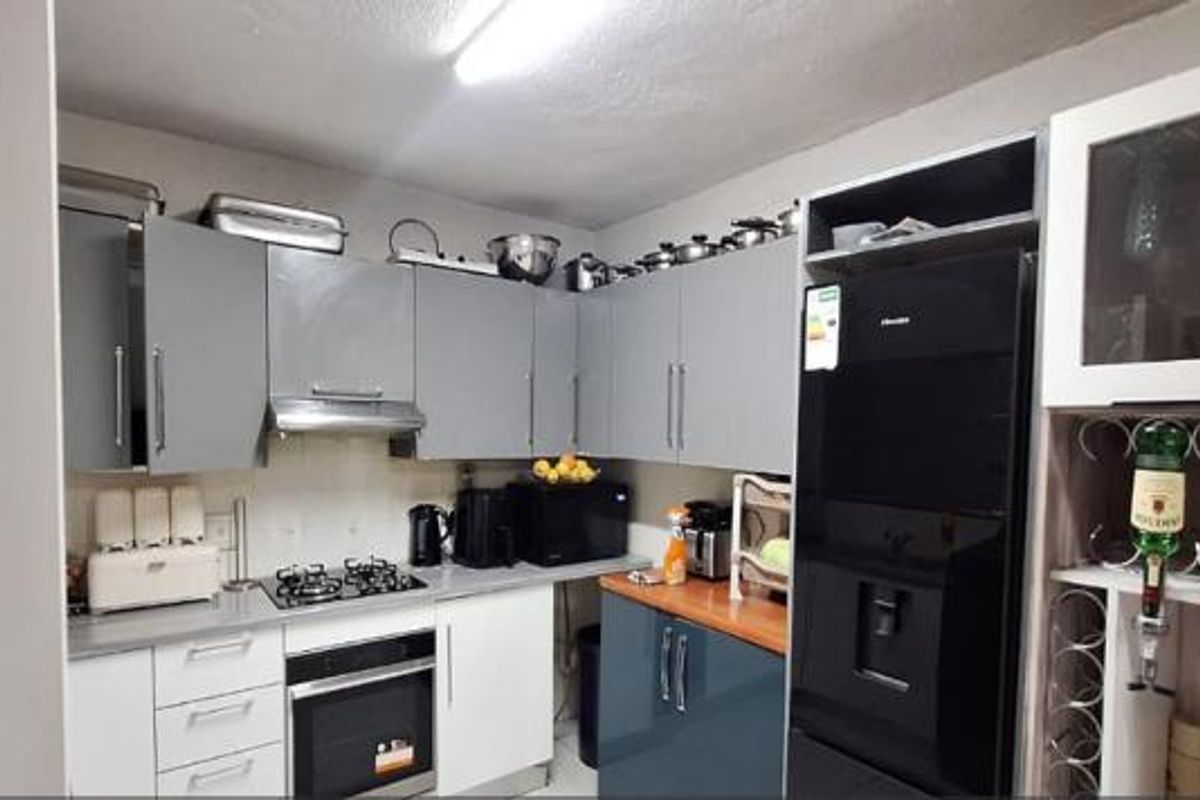 A functional kitchen featuring grey and white cabinetry, a gas hob with extractor fan, built-in oven, and a dedicated wine storage section.