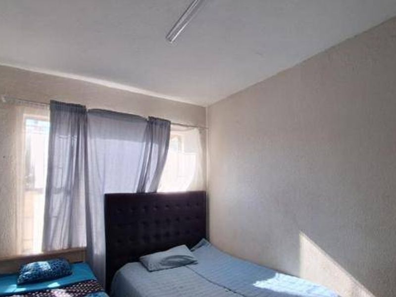 A functional bedroom featuring a window with a curtain rod and a ceiling-mounted light fixture.