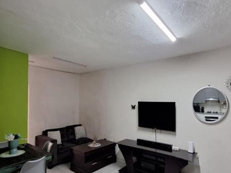 A living room area featuring tiled flooring and a basic ceiling light fixture, with a neutral wall palette and an accent green wall section.