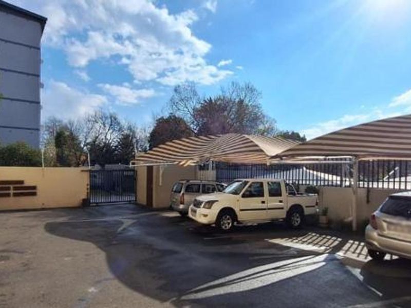 Exterior view of the apartment complex parking area featuring paved driveway and installed shade cloth carports for vehicle protection.