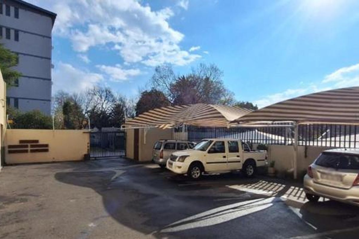 Exterior view of the apartment complex parking area featuring paved driveway and installed shade cloth carports for vehicle protection.