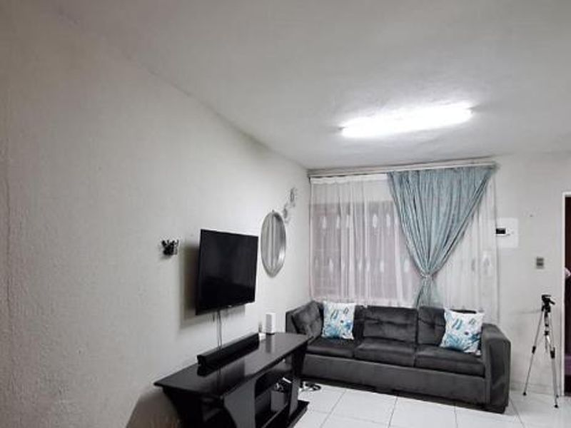 A living room area featuring tiled flooring and a security gate entrance, showing signs of wear on the wall surfaces.
