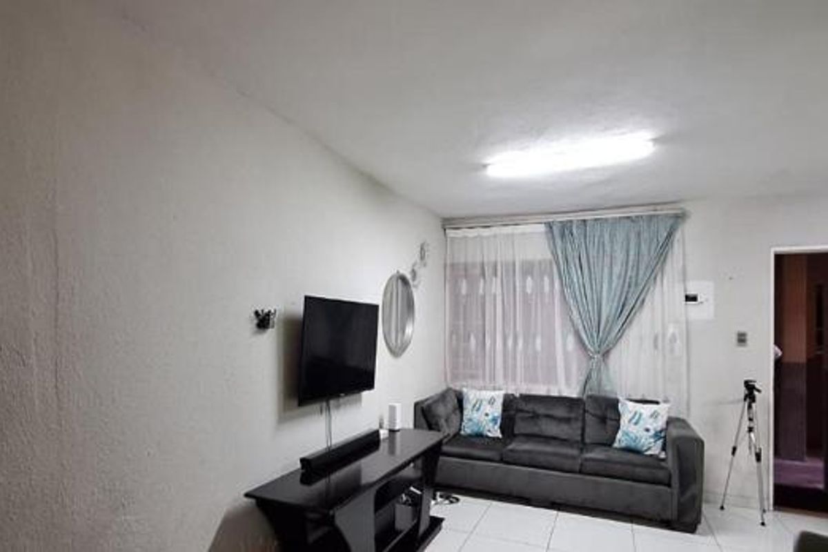 A living room area featuring tiled flooring and a security gate entrance, showing signs of wear on the wall surfaces.