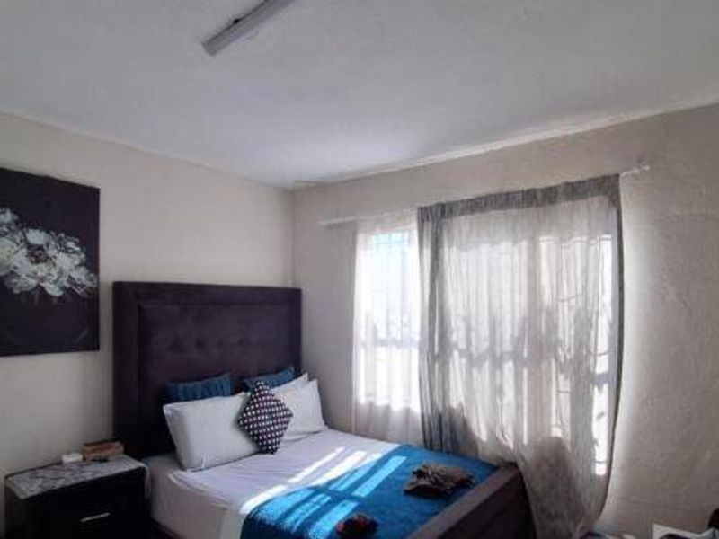 A bedroom featuring a window with security bars and textured wall finishes, offering a functional space with potential for cosmetic updates.