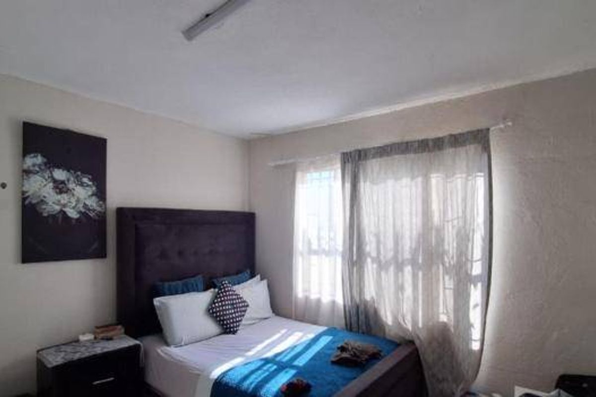 A bedroom featuring a window with security bars and textured wall finishes, offering a functional space with potential for cosmetic updates.