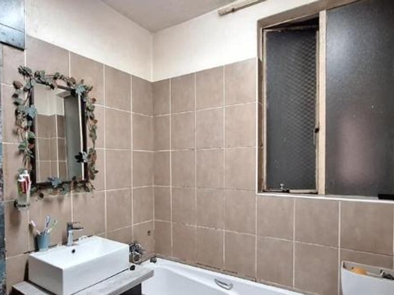 A bathroom featuring a vessel sink, bathtub, and tiled walls, requiring cosmetic updates to improve the overall aesthetic and condition of the space.