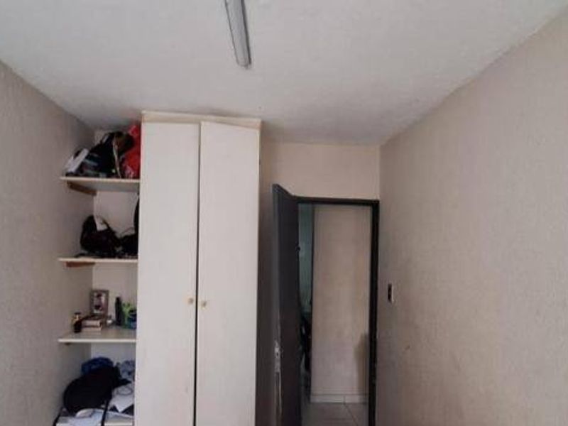 A compact bedroom featuring a built-in wardrobe and integrated shelving, requiring cosmetic updates to the walls and finishes.