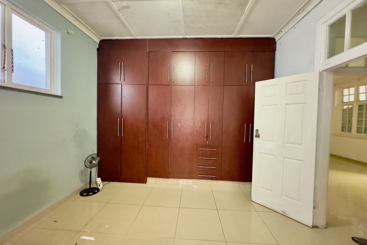 A spacious bedroom featuring extensive built-in wooden cupboards, tiled flooring, and a panelled ceiling, offering a blank canvas for personalization.