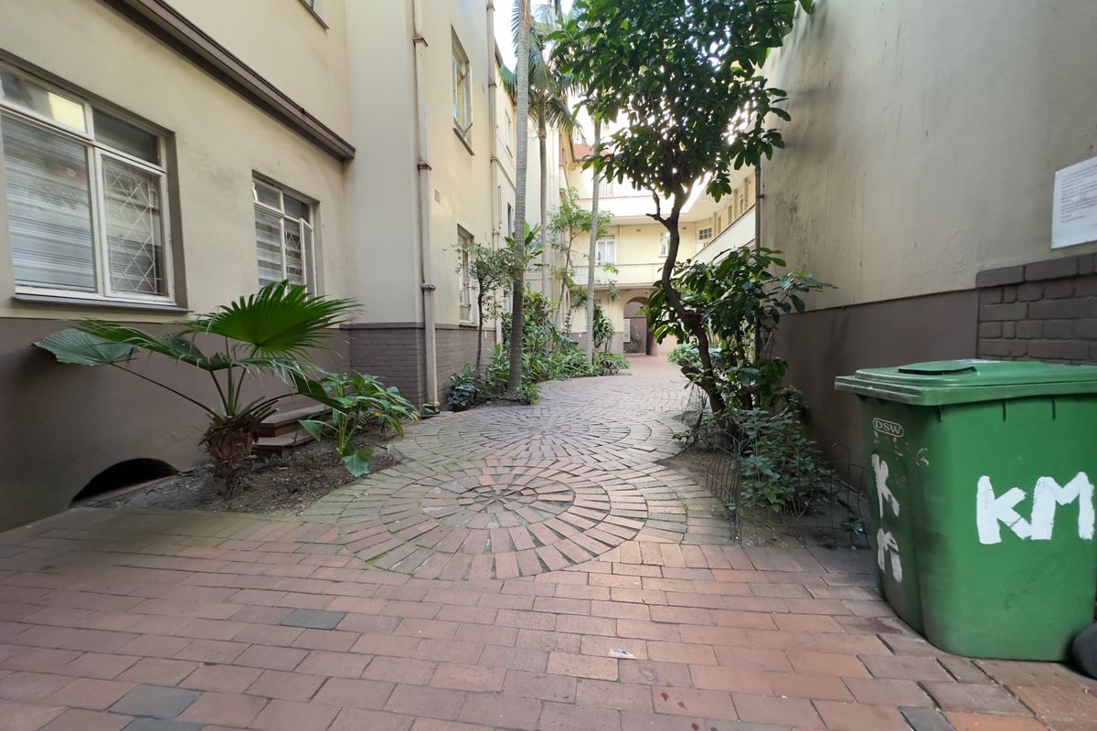 A view of the apartment complex's rear courtyard featuring brick paving and established garden landscaping between the building wings.