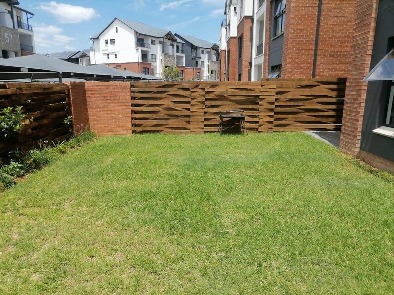 A private, well-maintained garden area featuring a manicured lawn, enclosed by a combination of brick walls and decorative timber slat fencing.