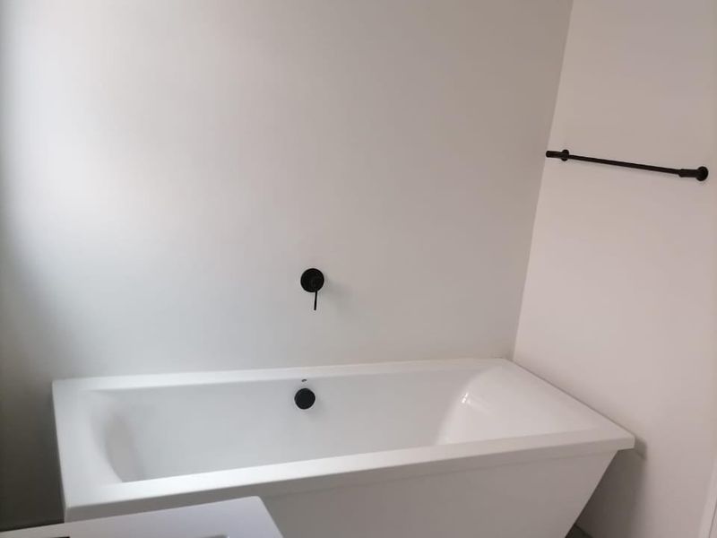Modern bathroom featuring a clean white freestanding bathtub, matte black fixtures, and neutral floor tiling in a minimalist, well-maintained space.