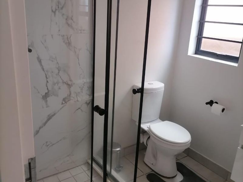 A clean, modern bathroom featuring a glass-enclosed shower with marble-look tiling, a white toilet, and neutral floor tiles.