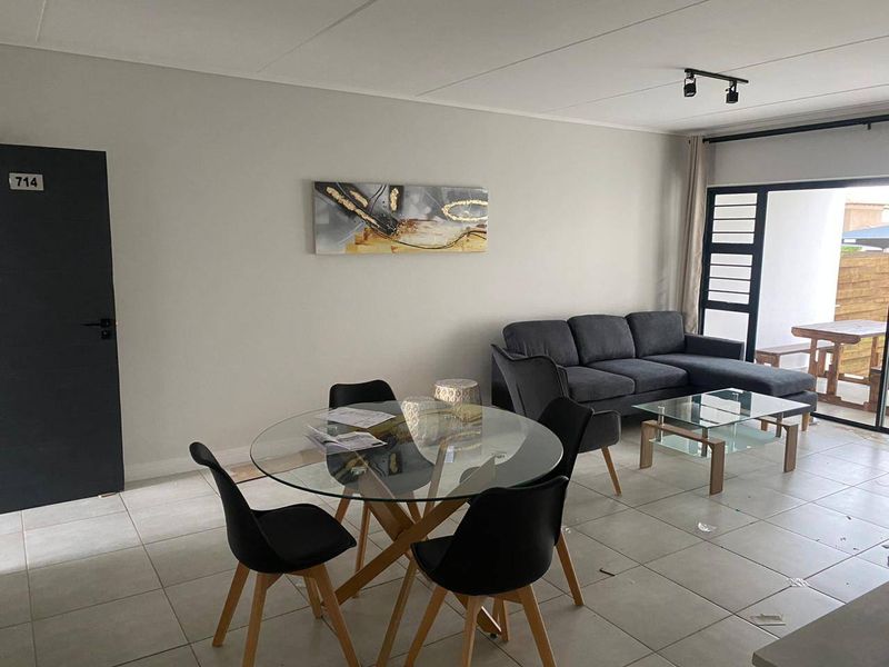 Open plan living and dining area featuring neutral tiled flooring, modern track lighting, and large sliding glass doors leading to an outdoor patio space.