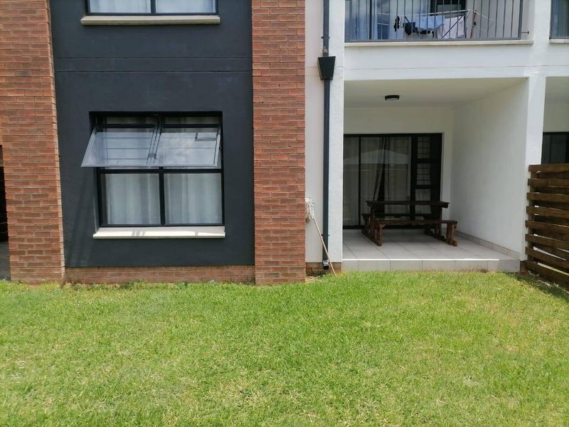 Rear view of an apartment building featuring a ground-floor tiled patio, brick and rendered facade, and a small private lawn area.