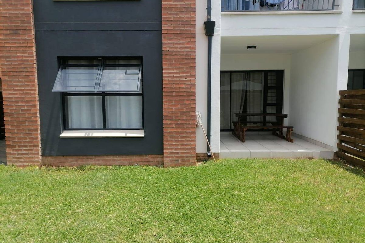 Rear view of an apartment building featuring a ground-floor tiled patio, brick and rendered facade, and a small private lawn area.
