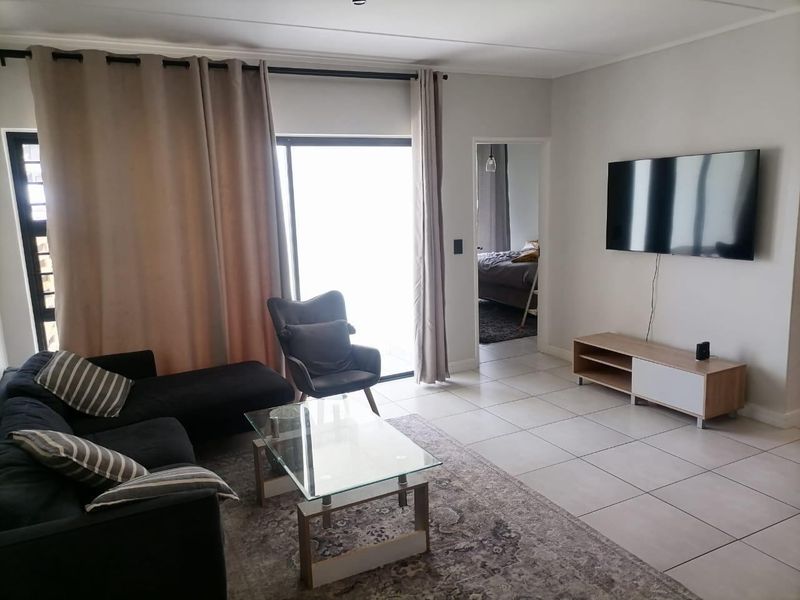 A bright living room featuring neutral tiled flooring and a sliding glass door providing access to the exterior.