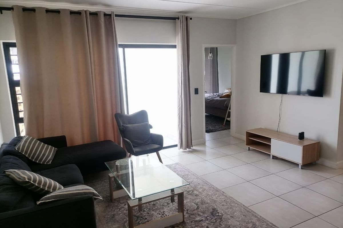 A bright living room featuring neutral tiled flooring and a sliding glass door providing access to the exterior.
