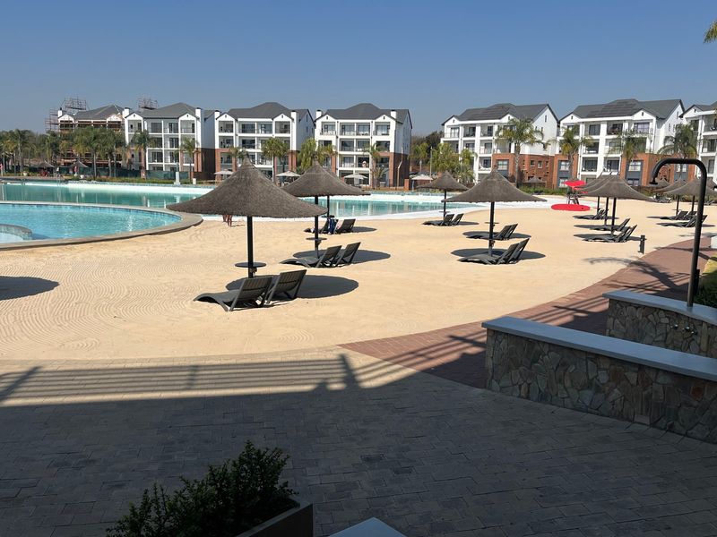 A well-maintained communal pool area featuring a sandy beach, paved patio, and stone-clad retaining walls within a modern apartment complex.