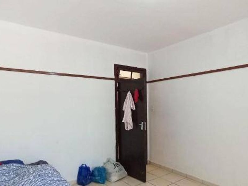 A simple, vacant bedroom featuring neutral white walls, a decorative wooden picture rail, and tiled flooring.