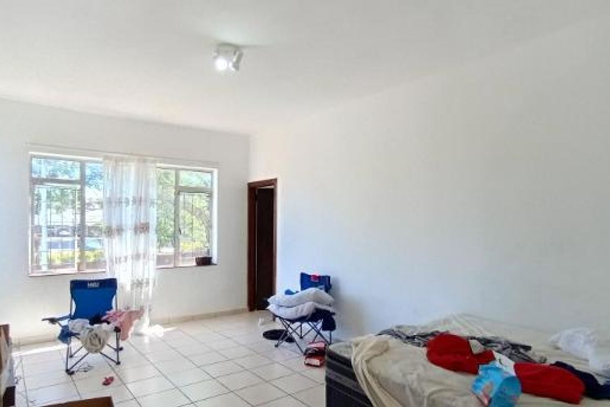A spacious, sunlit living area featuring neutral tiled flooring and large windows with security bars, offering a blank canvas for interior design.