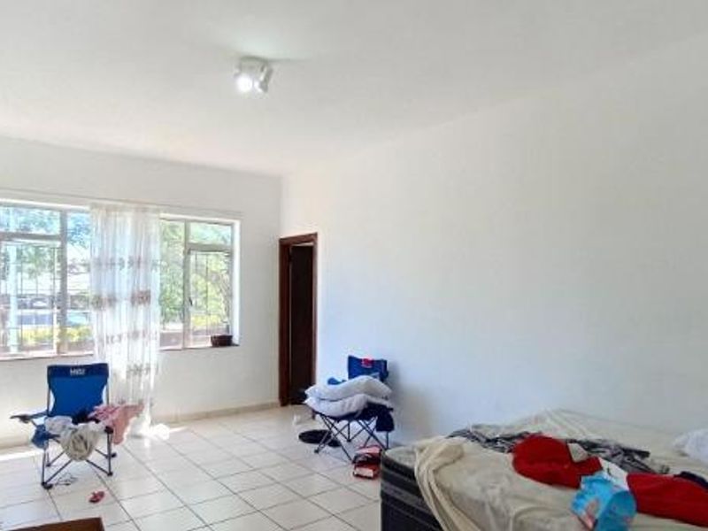 A spacious, sunlit living area featuring neutral tiled flooring and large windows with security bars, offering a blank canvas for interior design.