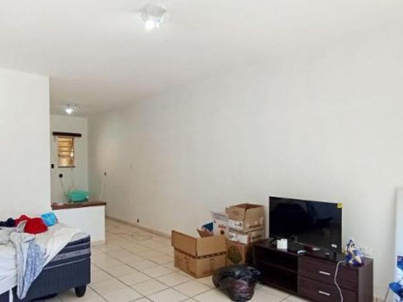 An open-plan living area featuring tiled flooring and a window with security bars, offering a functional space ready for personalization.