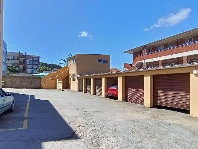 Rear exterior view of the apartment complex featuring a row of lock-up garages, paved driveway, and external staircase access.