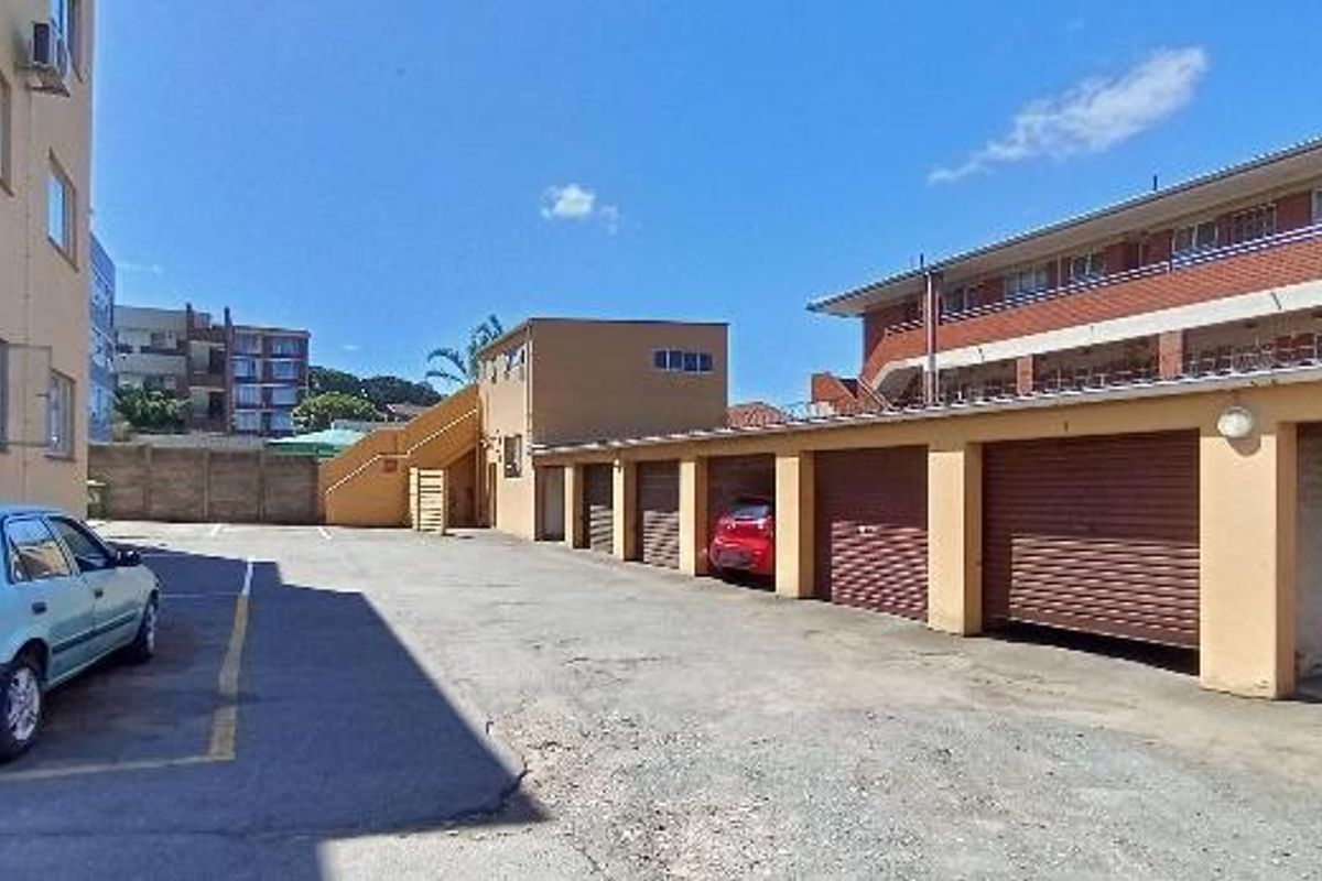 Rear exterior view of the apartment complex featuring a row of lock-up garages, paved driveway, and external staircase access.