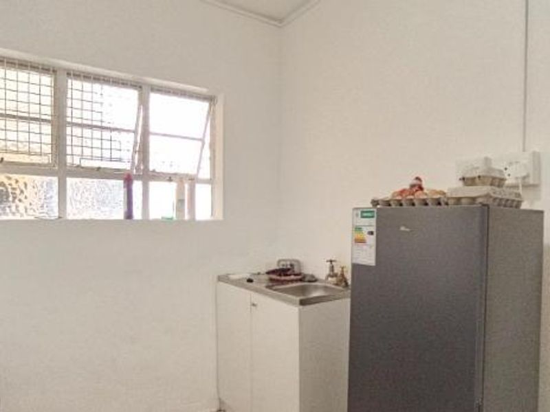A basic kitchen area featuring a small sink unit, cabinetry, and a window with security bars, requiring cosmetic updates to improve functionality and aesthetic appeal.