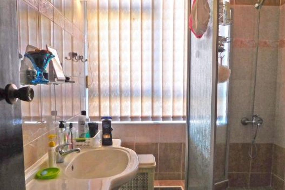 A functional bathroom featuring a pedestal washbasin, tiled wall finishes, and a glass-enclosed shower unit with a window providing natural light.