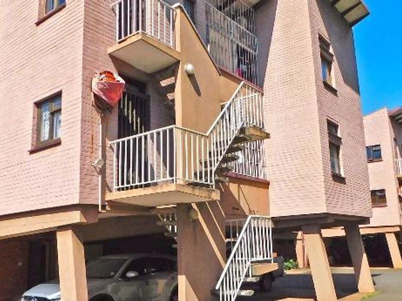 Exterior view of a multi-story apartment complex featuring brick facade, external staircases, and elevated stilt-style ground level parking.