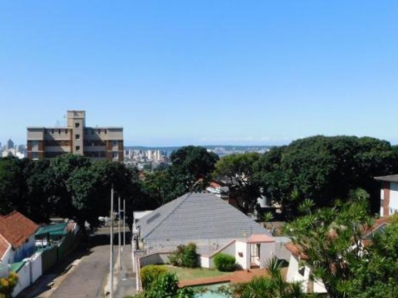 An elevated outdoor view overlooking the surrounding neighbourhood, mature trees, and distant city skyline.