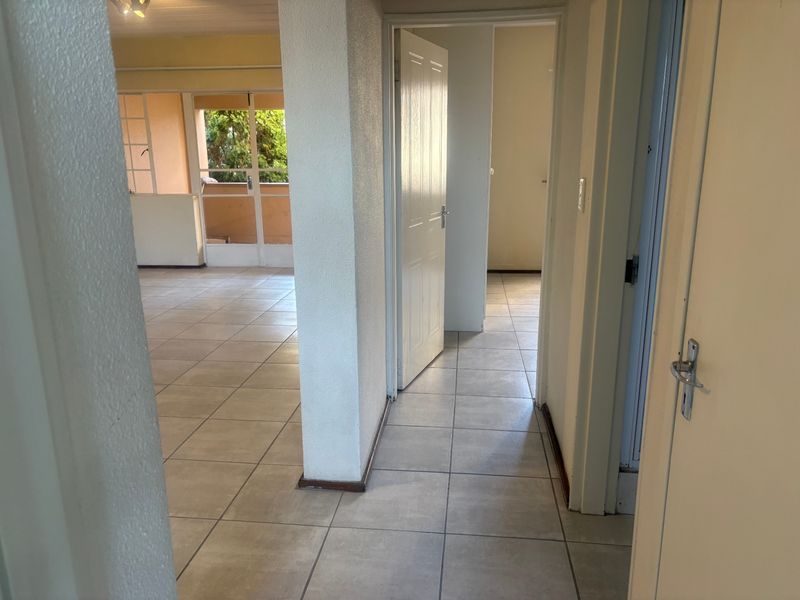 A bright, empty hallway with neutral tiled flooring, providing access to multiple rooms and connecting to an open-plan living area.