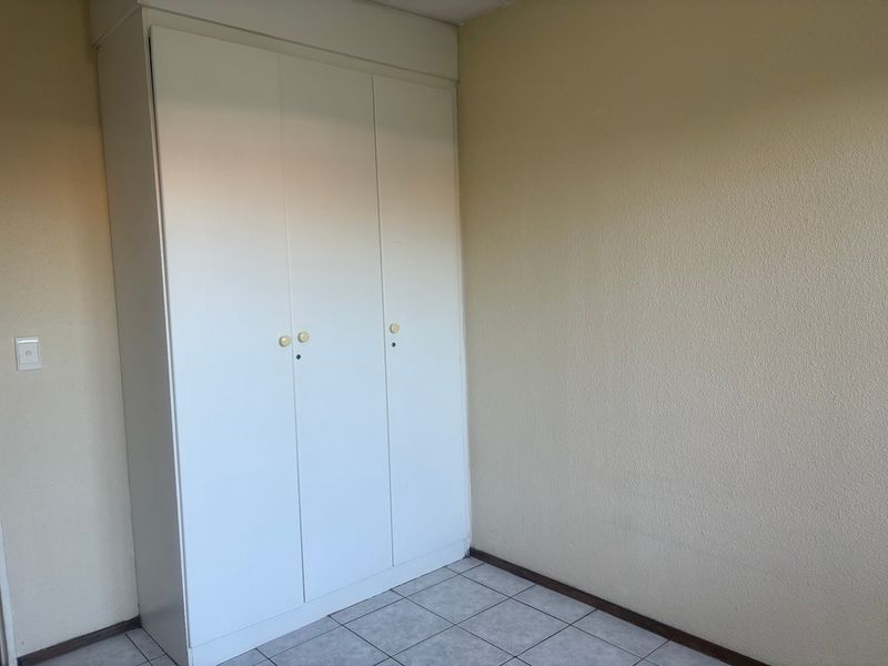 A simple bedroom featuring a white built-in wardrobe and tiled flooring, offering a clean and functional space ready for personalization.