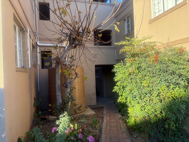 Rear exterior view of the apartment building featuring a brick pathway, water storage tank, and established garden area with visible wall maintenance required.